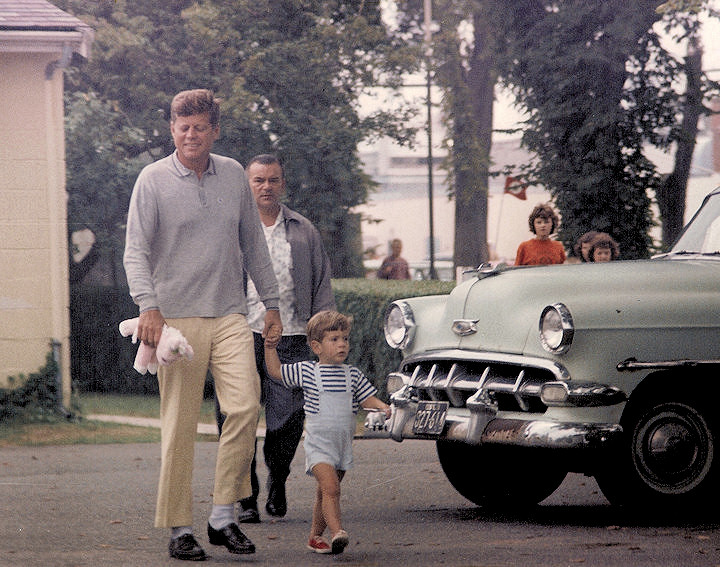 Été 1963 - Le président Kennedy sort d'un magasin de bonbons avec John Jr. en portant son animal jouet.