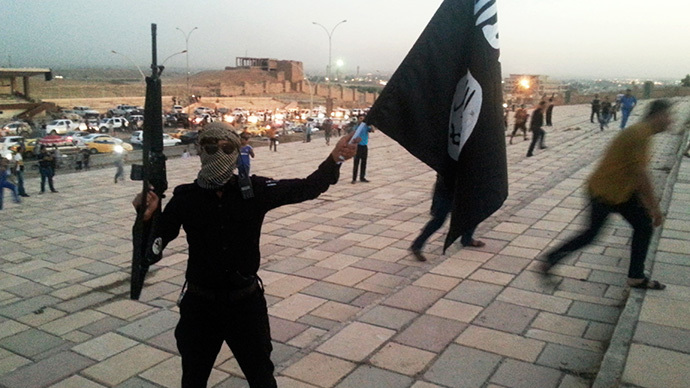 Un combattant de l'Etat islamique d'Irak et du Levant (ISIL) tient un drapeau de ISIL et une arme dans une rue de la ville de Mossoul